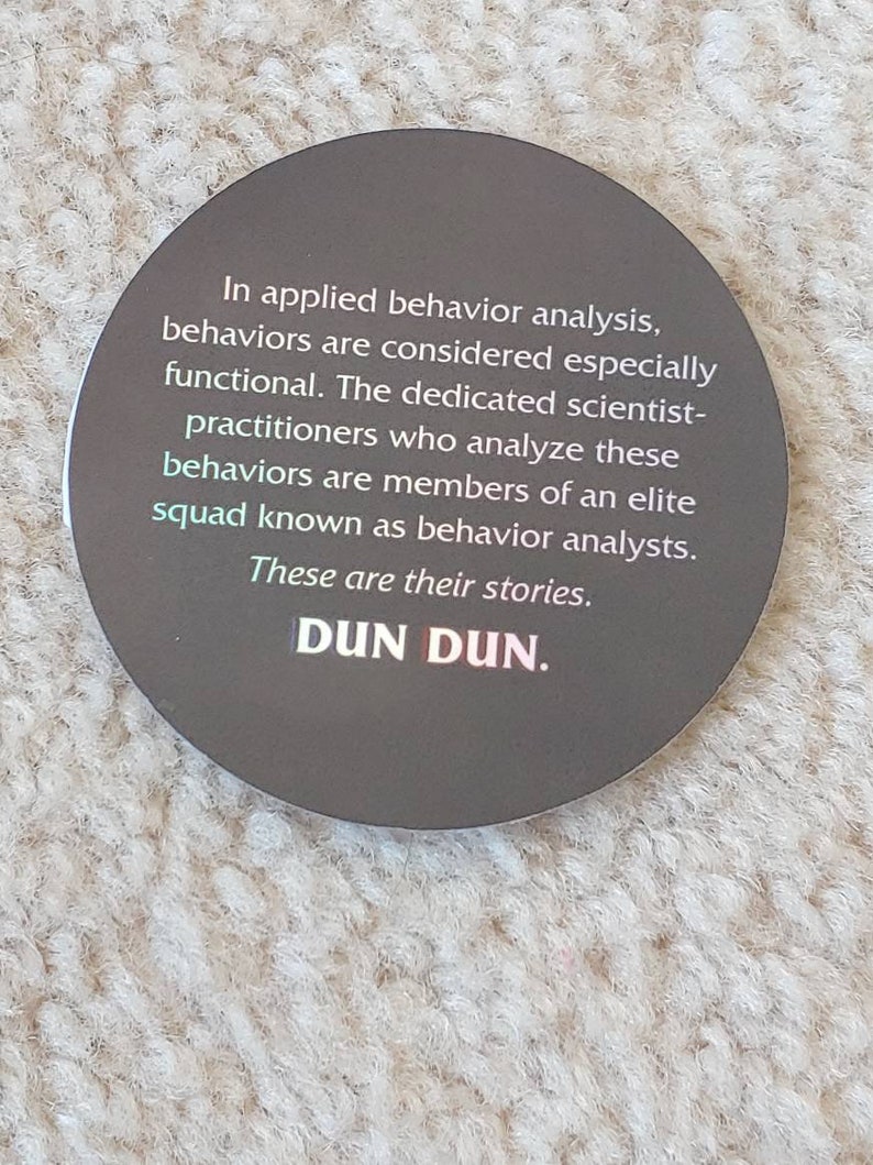 May include: A round sticker with a dark gray background and white text. The text reads: "In applied behavior analysis, behaviors are considered especially functional. The dedicated scientist-practitioners who analyze these behaviors are members of an elite squad known as behavior analysts. These are their stories. DUN DUN."