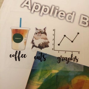 May include: A clear sticker featuring illustrations of a coffee cup, a cat, and a line graph. The word "coffee" is written below the cup, "cats" below the cat, and "graphs" below the graph. The coffee cup has a blue straw.