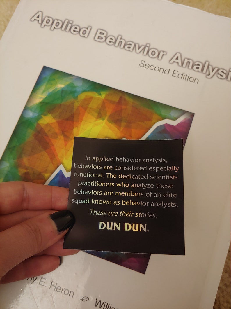 May include: A close-up of a black sticker with white text that reads "In applied behavior analysis, behaviors are considered especially functional. The dedicated scientist-practitioners who analyze these behaviors are members of an elite squad known as behavior analysts. These are their stories. DUN DUN."