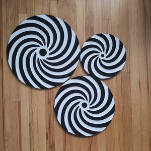May include: Three black and white spiral patterned round wall decor pieces. The largest piece is in the center and the two smaller pieces are on either side of it.