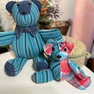 May include: Two handmade plush teddy bears. The larger bear is blue and white striped with a denim collar and bow tie. The smaller bear is blue and red plaid with a bow. Both bears have black button eyes.