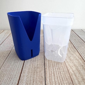 May include: A two-piece self-watering planter set consisting of a solid blue outer container with a V-shaped cutout and a vertical slot, and a clear, translucent inner liner with a white wick extending from the bottom for water absorption.
