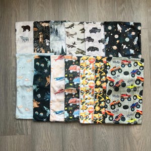 May include: A collection of baby blankets with various patterns. Designs include bears, forests, airplanes, trucks, space, and monster trucks. The blankets are made of soft fabric and are suitable for infants and toddlers.