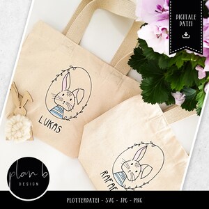 May include: Two beige tote bags with black bunny illustrations and the names "Lukas" and "Rafael" printed on them. The bags have white handles and are lying on a white surface.