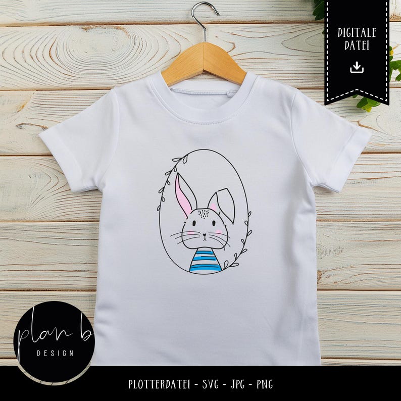 May include: White t-shirt featuring a black and white illustration of a bunny in an oval frame with leaves. The bunny has pink ears and blue and white stripes on its chest. The text "DIGITALE DATEI" is in a black box with a download icon.