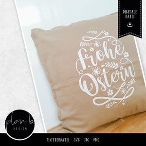 K&ouml;nnte beinhalten: Ein beiger Kissenbezug mit wei&szlig;em Text, der "Frohe Ostern" mit einem floralen Design lautet. Das Kissen ist eine digitale Download-Datei.