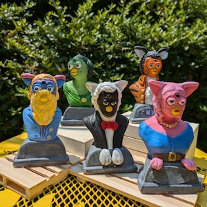 May include: Five colorful ceramic busts of cartoon characters, each with a unique design and expression. The busts are displayed on wooden platforms, creating a whimsical and playful scene.