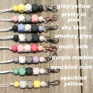 May include: A set of 8 silicone teething necklaces with different color combinations and patterns. The necklaces are made with a variety of colors, including grey, yellow, pink, blue, and mint. Each necklace has a metal clasp and a white cord.