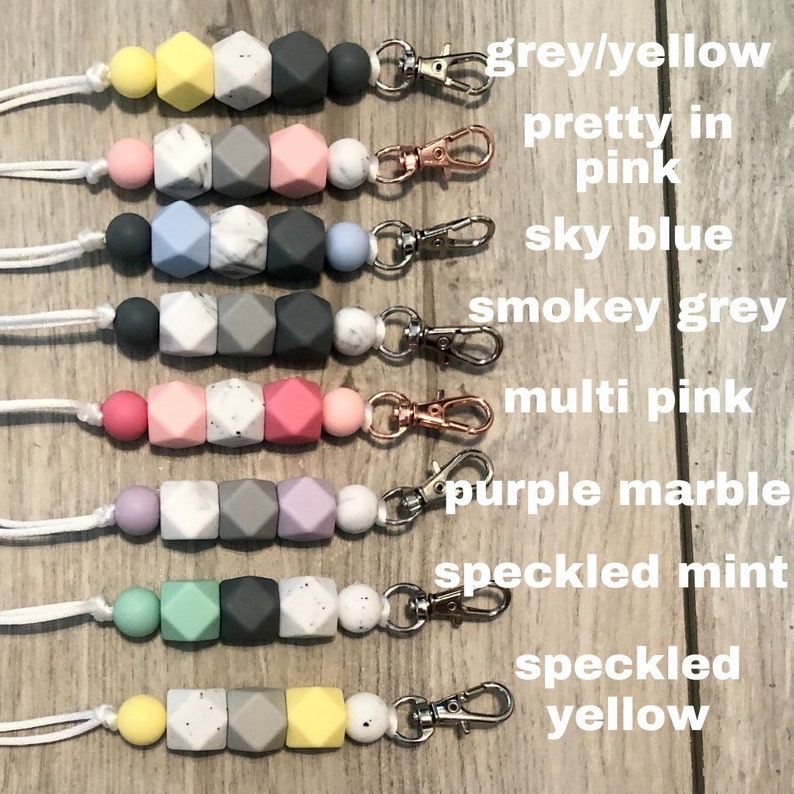 May include: A set of 8 silicone teething necklaces with different color combinations and patterns. The necklaces are made with a variety of colors, including grey, yellow, pink, blue, and mint. Each necklace has a metal clasp and a white cord.