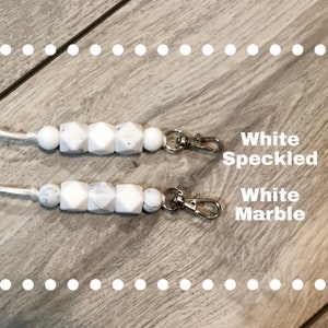 May include: Two white silicone keychains with silver clasps. The top keychain has white beads with black speckles. The bottom keychain has white beads with a marble pattern. The text "White Speckled" and "White Marble" is written below each keychain.