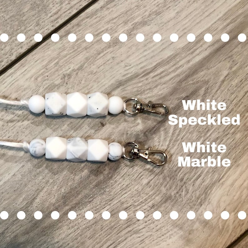 May include: Two white silicone keychains with silver clasps. The top keychain has white beads with black speckles. The bottom keychain has white beads with a marble pattern. The text "White Speckled" and "White Marble" is written below each keychain.