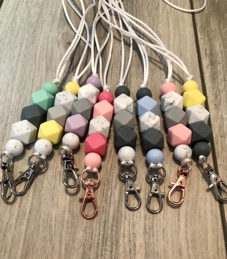 May include: A set of seven colorful silicone beaded lanyards with a white cord and a silver or rose gold lobster clasp. The beads are in various colors, including light blue, pink, yellow, gray, and green.