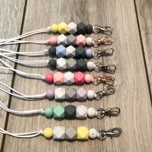 May include: Eight silicone bead keychains with white cords. The beads are in various colors, including yellow, pink, blue, purple, green, and gray. Each keychain has a silver or gold metal clasp.