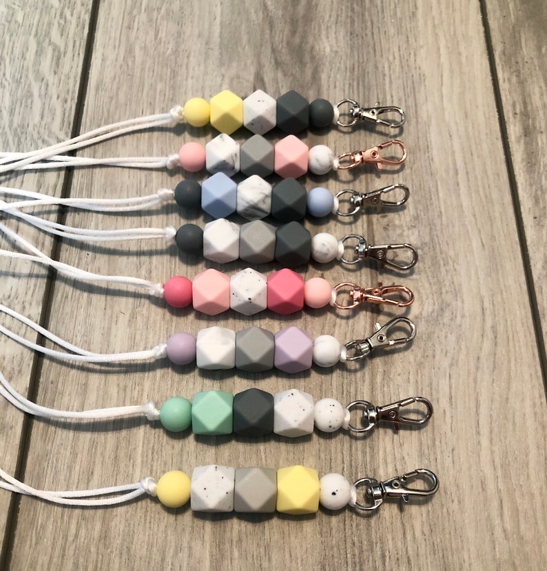 May include: Eight silicone bead keychains with white cords. The beads are in various colors, including yellow, pink, blue, purple, green, and gray. Each keychain has a silver or gold metal clasp.