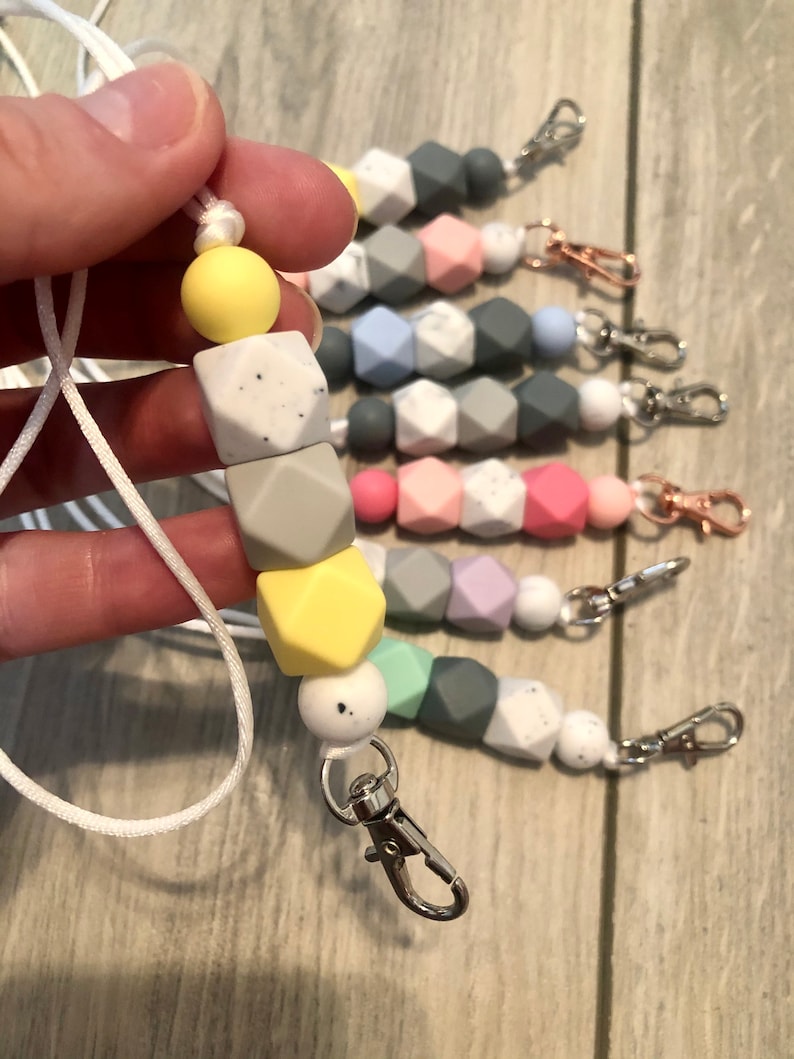 May include: A white cord with a silver clip and a string of colorful silicone beads. The beads are in various shades of gray, yellow, green, and pink. The beads have a speckled pattern.