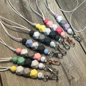 May include: A set of seven colorful silicone bead lanyards with silver and gold lobster clasps. Each lanyard features a different color combination of beads, including pastel pink, light blue, gray, white, and yellow.