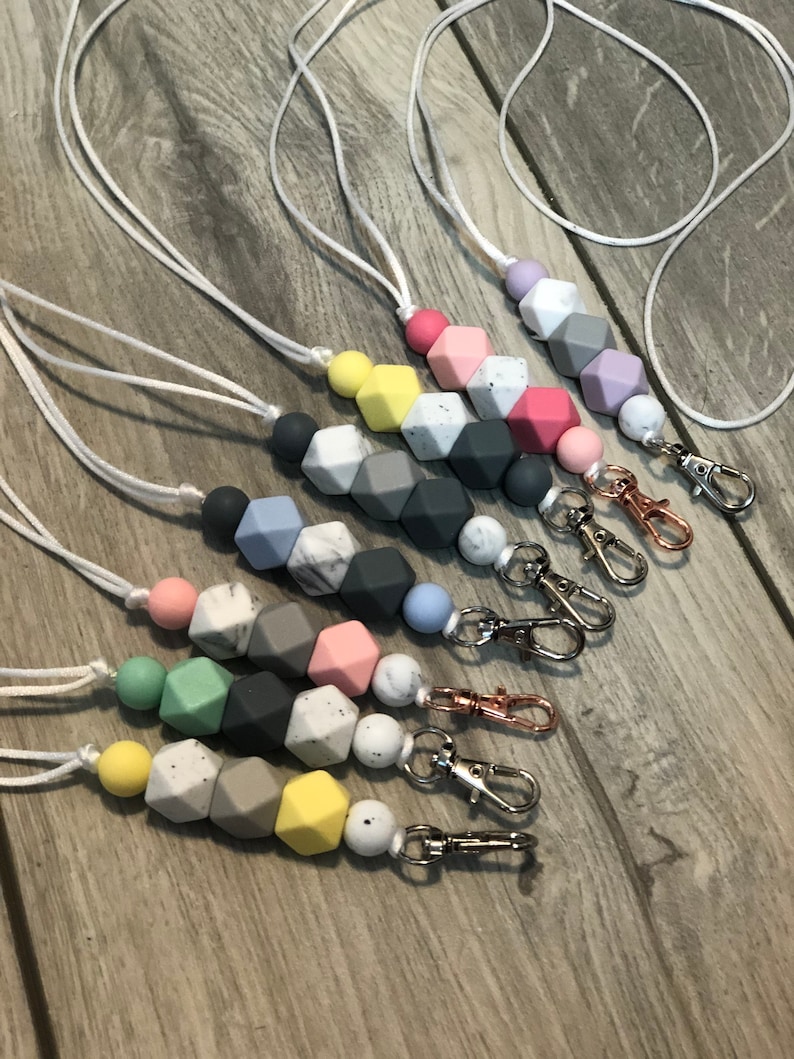 May include: A set of seven colorful silicone bead lanyards with silver and gold lobster clasps. Each lanyard features a different color combination of beads, including pastel pink, light blue, gray, white, and yellow.