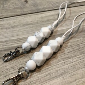 May include: Two white silicone beaded lanyards with silver lobster clasps. The beads are white with a marbled pattern.
