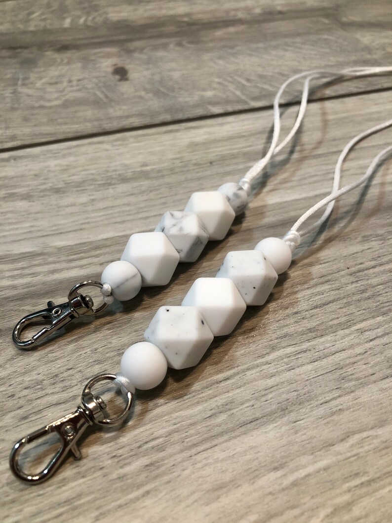 May include: Two white silicone beaded lanyards with silver lobster clasps. The beads are white with a marbled pattern.