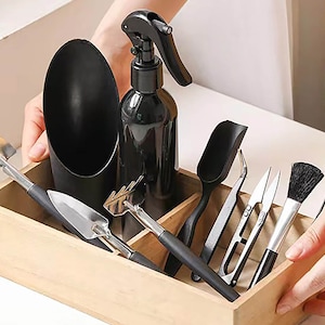 May include: A wooden box containing a selection of gardening tools, including a trowel, a rake, a pair of tweezers, a small pair of scissors, a brush, and a black plastic watering bottle.