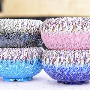 Puede incluir: Cuatro macetas de cerámica en diferentes colores, apiladas en pares. Las macetas tienen un esmalte texturizado craquelado en tonos de azul, rosa y negro.