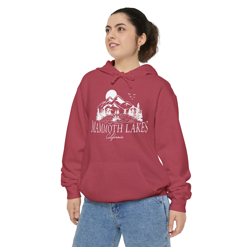 以下が含まれることがあります： 山、湖、木々が描かれた白いグラフィックと「Mammoth Lakes California」の文字が入った、マルーン色のフード付きスウェットシャツ。スウェットシャツにはフロントポケットとドローストリングフードが付いています。