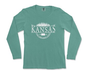 May include: A teal long-sleeve t-shirt with a white graphic design featuring the word "Kansas" with a silhouette of trees and the text "The Sunflower State" with the years 1861.