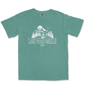 May include: A teal blue t-shirt with a white graphic of a mountain range, lake, and the text "LAKE PEND OREILLE Idaho".