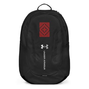 May include: Black backpack featuring a red and white geometric pattern. The Under Armour logo is silver, with the words "Under Armour" in white. The bag has a top handle and mesh side pockets. Ideal for carrying essentials.