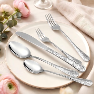 May include: A set of four stainless steel utensils including a dinner fork, a smaller fork, a dinner knife, and two spoons, all featuring intricate embossed floral scrollwork patterns on the handles and polished, smooth, reflective bowls and tines.