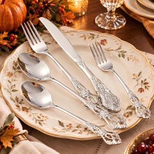 May include: A five-piece silver-toned flatware set consisting of a dinner fork, a dinner knife, a salad fork, a soup spoon, and a teaspoon. Each piece features an ornate, embossed floral handle design with a polished, reflective metallic finish.