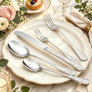May include: A set of four silver-toned stainless steel flatware pieces including a dinner fork, a salad fork, a dinner knife, and two spoons. Each handle features an intricate, embossed scrollwork pattern with a polished, reflective finish.