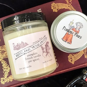 May include: A 7 ounce soy candle in a clear glass jar with a black lid. The label is white with black text and a black and white illustration of a building. The text on the label reads "Pestilence Pours Bring Out Your Dead pumpkin french vanilla pie spices made in oregon".