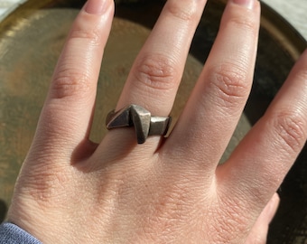 May include: A silver ring with a geometric design. The ring is worn on a person's finger.
