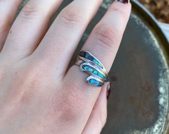 May include: A silver ring with a blue and green abalone inlay. The ring is designed with a wavy, organic shape.