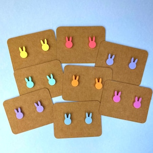 May include: Assortment of bunny shaped stud earrings on brown card stock. The earrings are in various pastel colours including pink, blue, yellow, orange, and green.
