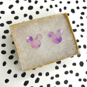 May include: A pair of purple and white mouse ear shaped stud earrings in a small brown box with white tissue paper.