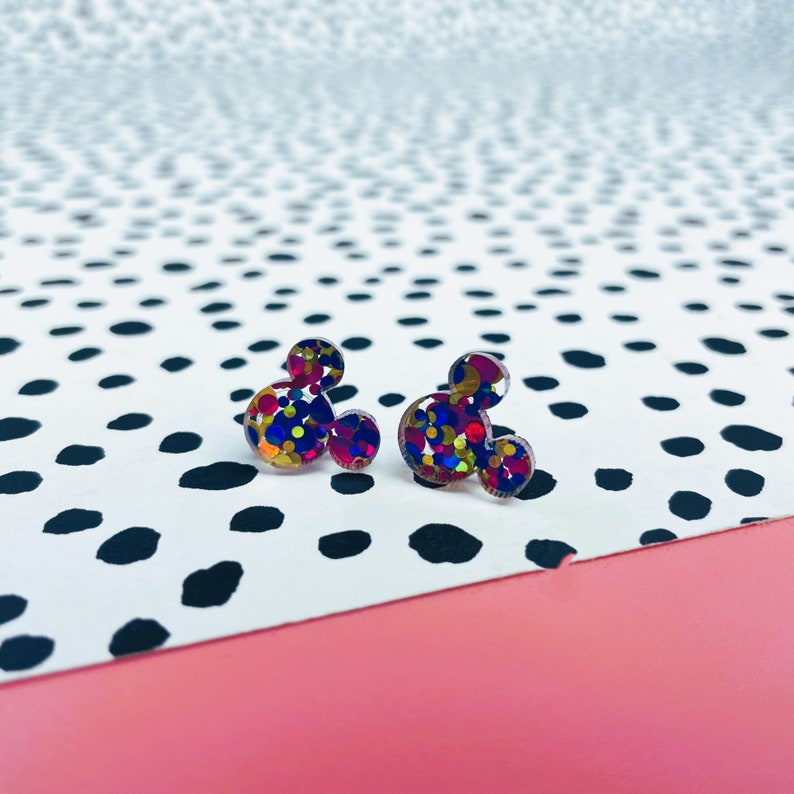 Puede incluir: Un par de pendientes con forma de Mickey Mouse con confeti de colores. Los pendientes est&aacute;n hechos de resina transparente con purpurina incrustada en tonos rojos, azules, amarillos y dorados.