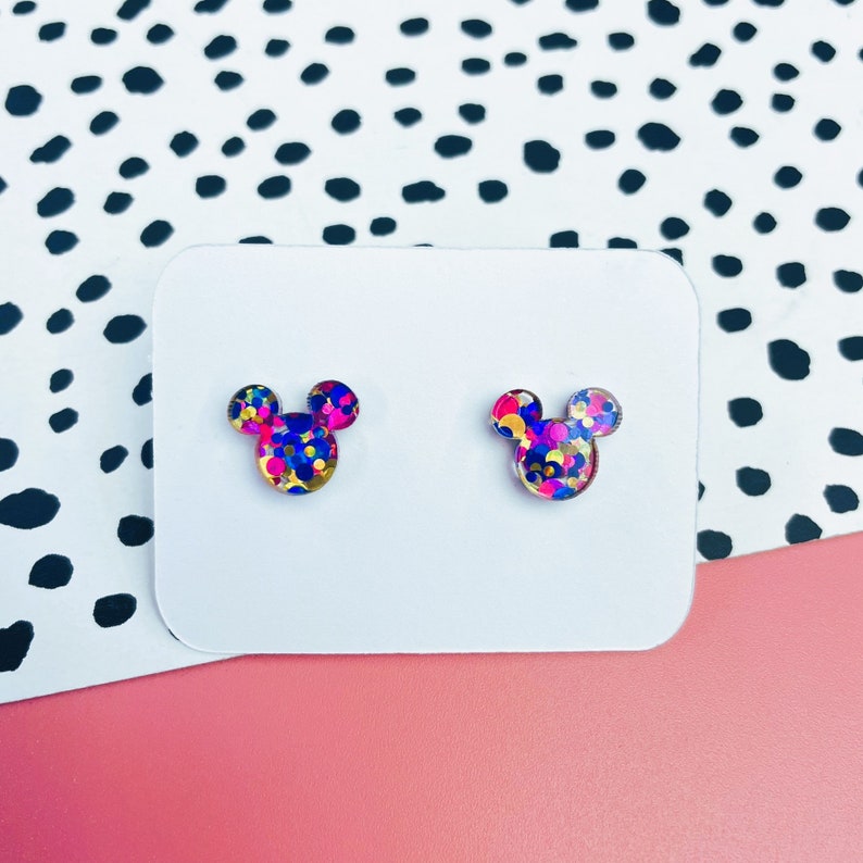 Puede incluir: Un par de pendientes de bot&oacute;n con una silueta de Mickey Mouse llena de confeti de colores. El confeti es rosa, azul, amarillo y dorado.