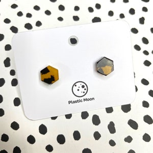May include: A pair of hexagonal stud earrings with a tortoiseshell pattern. The earrings are on a white card with the text "Plastic Moon".