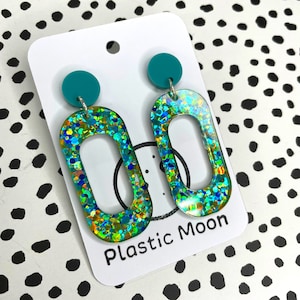 May include: Teal and iridescent glitter oval shaped earrings with a teal circle at the top. The earrings are on a white card with the text "Plastic Moon".