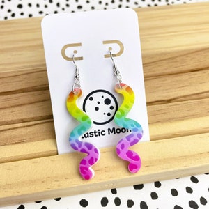 Peut inclure: Boucles d'oreilles pendantes en forme de spirale arc-en-ciel sur fond blanc. Les boucles d'oreilles sont en plastique et ont un motif léopard. Les boucles d'oreilles sont suspendues à des crochets argentés.