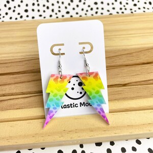 May include: Rainbow lightning bolt earrings with a leopard print pattern. The earrings are silver and have a hook fastening.