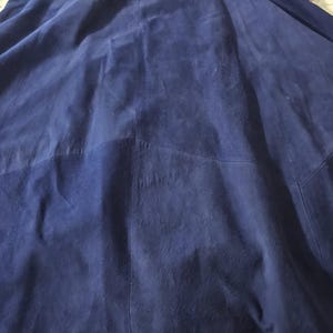 May include: A dark blue suede skirt featuring a multi-panel construction with visible vertical seams. A white measuring tape is positioned across the top waistband, showing a measurement of approximately 16 inches across the waist area.