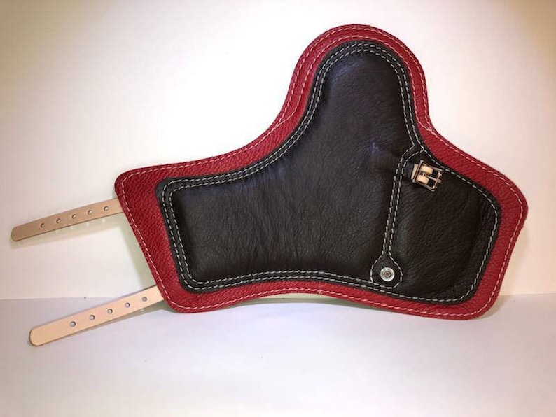 Pu&ograve; includere: Un ginocchiere in pelle rossa con un inserto in pelle nera e dettagli di cucitura bianca. Il ginocchiere ha due cinturini con fibbie.