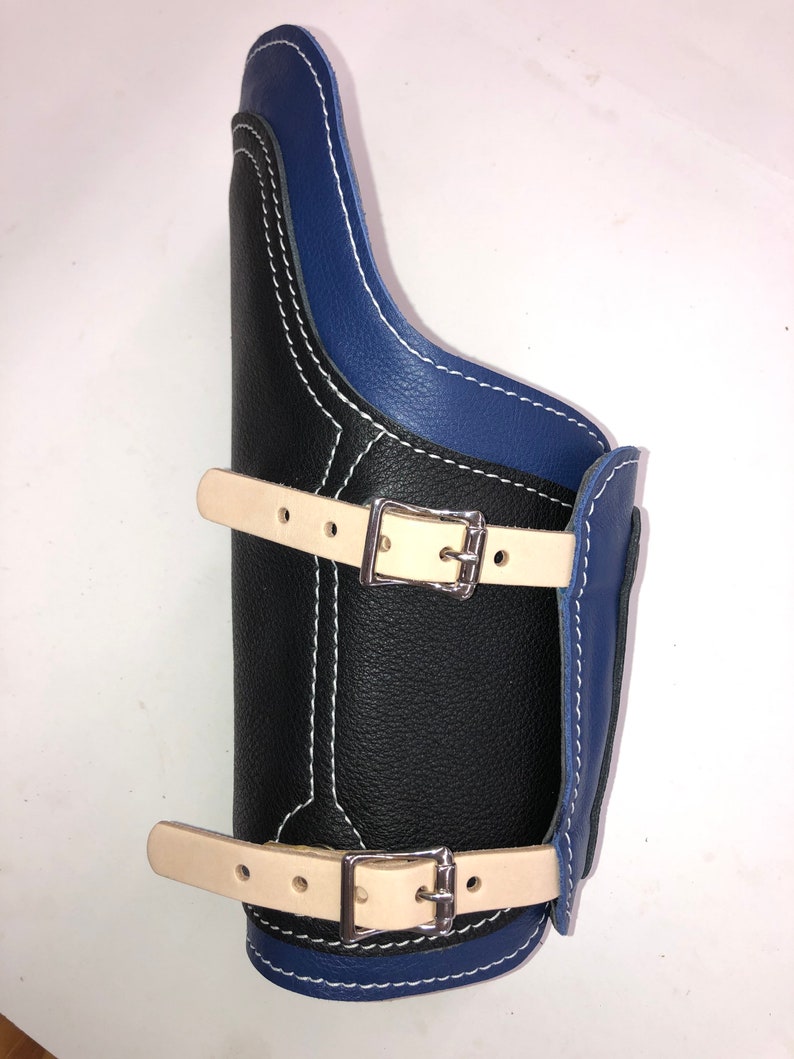 Pu&ograve; includere: Un proteggi-avambraccio in pelle nera con bordatura in pelle blu e due cinturini regolabili con fibbie argentate.