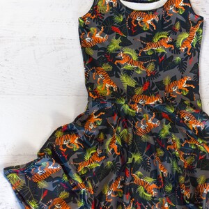 May include: A sleeveless dress with a black background and a pattern of orange tigers and green leaves.