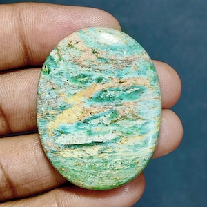 May include: An oval-shaped polished gemstone featuring a marbled pattern of vibrant turquoise, mint green, and creamy beige streaks. The stone has a smooth, glossy surface with a natural, irregular texture visible beneath the polished finish.