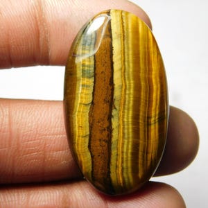 May include: A large, oval-shaped, polished tiger's eye gemstone with a golden brown color and a distinctive chatoyancy effect. The stone has a smooth, glossy finish and exhibits a variety of brown, gold, and black stripes.