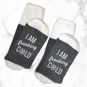 May include: Pair of gray and white socks with the text "I am freaking cold" and a snowflake on each sock.